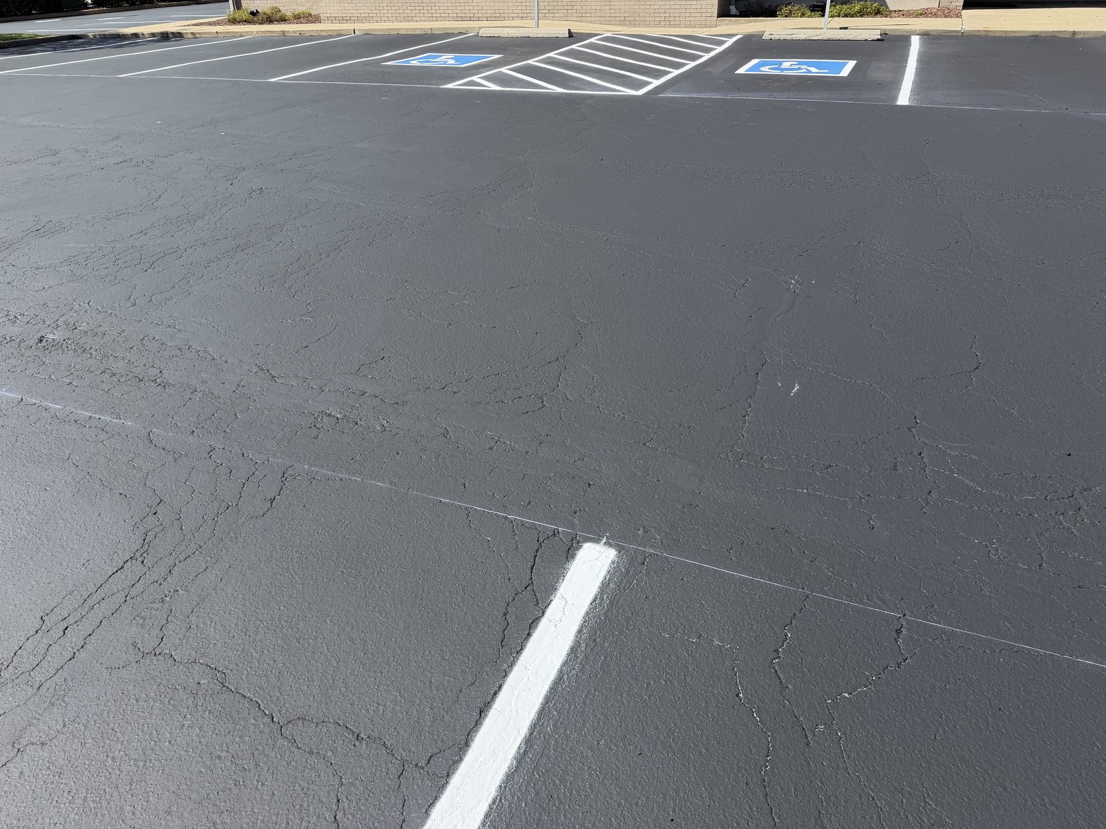 A commercial parking lot freshly sealcoated and restriped, with new accessible parking stalls